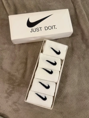 Vita Nike strumpor i box - Säljer ett 5-pack vita ribbade strumpor från Nike med klassisk svart swoosh-logga. Strumporna kommer i originalbox och är perfekta för dig som gillar sportig och clean stil. 36-42