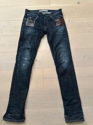Mörkblå jeans med läderdetaljer - Sjuuukt feta Denim Replay Jeans med otrolig wash och galna detaljer som syns på bilderna. Jeansen är klippta ner till vilket ger dem en flare look. Storlek W28 isch. Känner inte att jag behöver beskriva alla coola designer så det är bara för dig att kolla på bilderna!  Skriv om du har några funderingar!!! 