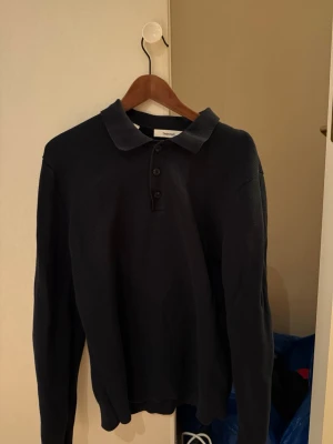 Mörkblå pikétröja med krage - Snygg mörkblå långärmad pikétröja från Selected Homme. Tröjan har klassisk krage och tre knappar framtill. Tillverkad i ett mjukt, stickat material som ger en avslappnad men stilren look.