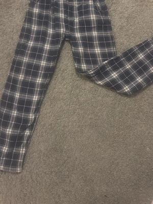 Rutiga pyjamasbyxor i bomull - Mysiga pyjamasbyxor med svart, vitt och grått rutmönster. Tillverkade i mjuk bomull med avslappnad passform och långa ben. Perfekta för chillkvällar hemma.
