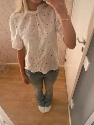 Vit broderad blus - Superfin vit blus med broderade detaljer och hålmönster. Blusen har puffiga korta ärmar och en söt volang vid halsen. 