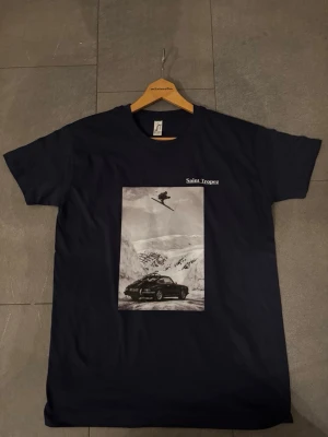 Svart Saint Tropez t-shirt med tryck - Cool navi blue t-shirt från Saint Tropez med ett stort svartvitt tryck på bröstet som visar en skidåkare och en bil i ett snöigt landskap. Klassisk rund hals och korta ärmar. Perfekt för dig som ska på afterski. har dom i (S) och (M) skynda och köp har inte många kvar