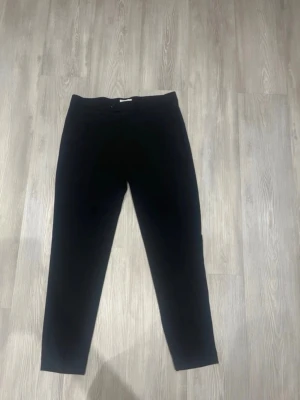 Svarta Lindbergh kostymbyxor - Snygga svarta kostymbyxor med smal passform och klassisk midja. Byxorna har raka ben och diskreta fickor i sidorna. Perfekta för en stilren look och passar till skjorta eller t-shirt. Materialet känns mjukt och följsamt.