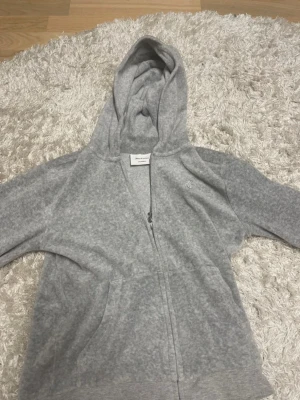 Juicy conture grå kofta  - Mjuk och skön grå kofta  med dragkedja framtill och två fickor.Perfekt för chill dagar eller när du vill ha en enkel och stilren look. Tillverkad i bomullsblandning. Äkta kofta . Nypris 1500 kr. Fel storlek , så aldrig kommit till användning! 💞