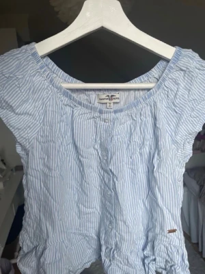 Blåvit randig blus Hampton republic - Söt blus från Hampton Republic i blåvitt randigt bomullstyg. Modellen har korta ärmar, rund halsringning och knappar framtill. Jättefin till sommaren