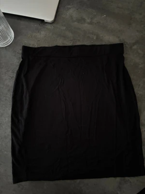 Svart enkel kortkjol - En svart, enkel och stilren kortkjol i mjukt material. Kjolen har en rak passform och resår i midjan, vilket gör den bekväm och lätt att matcha med olika outfits. Perfekt basplagg för garderoben.