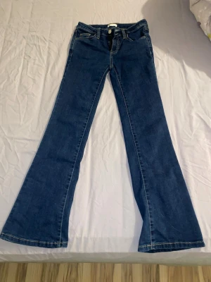 Mörkblå bootcut jeans - Säljer ett par mörkblå bootcut jeans med klassisk femficksdesign och kontrastsömmar. Jeansen har utsvängda ben och lite högmidja, perfekta för en trendig och avslappnad look. Materialet är klassisk denim i bomull.