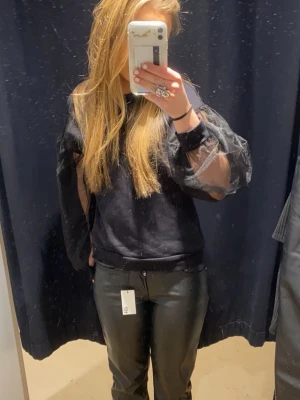 Svart topp med meshärmar - Trendig svart topp med transparenta meshärmar och puffdetaljer. Rund halsringning och avslappnad passform. Perfekt för dig som vill ha en cool och modern look.