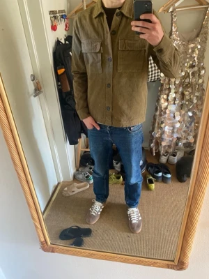 Olivgrön overshirt från Studio Total - Säljer en stilren olivgrön overshirt från Studio Total. Skjortjackan har två stora bröstfickor med lock, knäppning framtill och rak passform. Tillverkad i ett mjukt bomullstyg som ger en avslappnad men snygg look.