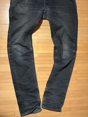 Svarta slim fit jeans från Nudie - Säljer ett par svarta Tim grim jeans från Nudie Jeans med klassisk femficksmodell och diskreta slitningar. Jeansen har raka ben och är tillverkade i mjuk denim med tydliga sömmar. Perfekta för en avslappnad och stilren look.