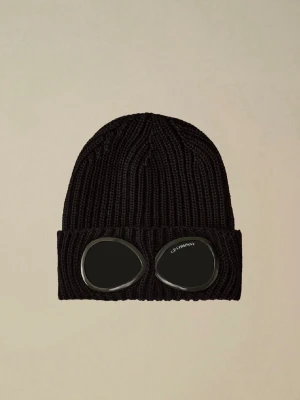Svart mössa med goggles från C.P. Company - Säljer en svart ribbstickad mössa från C.P. Company med ikoniska inbyggda goggles på uppviket. Mössan är gjord i tjockt, mjukt material och har en cool streetwear-vibe. Perfekt för dig som vill sticka ut och gillar unika accessoarer.