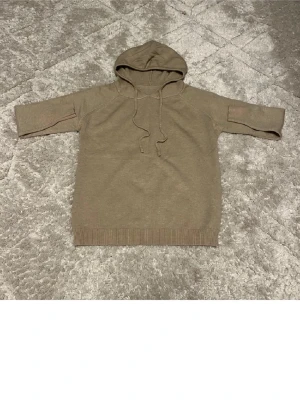 Beige stickad hoodie med huva - Säljer en beige stickad hoodie med huva och dragsko. Hoodien har ribbade muddar vid nederkant och ärmar, samt en avslappnad passform. Perfekt för dig som gillar en enkel och stilren look. Materialet känns mjukt och skönt mot huden.