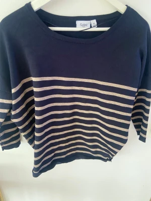 Marinblå randig tröja från Saint - Snygg marinblå tröja från Saint med beigea horisontella ränder över bröstet och ärmarna. Tröjan har rund halsringning och trekvartsärmar.