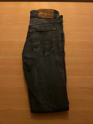 Tiger of Sweden jeans  - ALDRIG ANVÄNDA! Tiger of Sweden Säljer ett par mörkblå jeans med klassisk femficksdesign och en snygg skinnpatch i midjan. Jeansen har raka ben och diskreta sömmar, perfekta för en clean och enkel look. Materialet är slitstarkt denim i bomull.