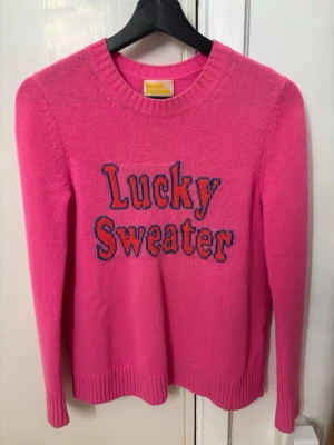 Rosa Lucky Sweater från From Future - Stickad karshmir tröja i rosa från From Future med texten 'Lucky Sweater'. Tröjan har rund halsringning och långa ärmar. Den är använd men behållen i bra skick, tror den är köpt i strl S men lite uttöjd - skulle säg att den är mer som s/m. Äldre model som inte finns kvar i produktion längre, nypris mellan 2500-3500 kr