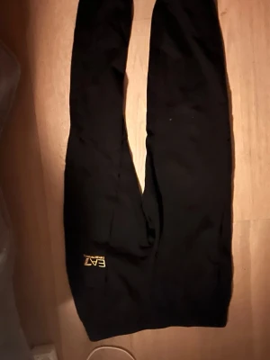 Svarta mjukisbyxor från EA7 - Snygga svarta mjukisbyxor från EA7 Emporio Armani med gul logga på benet. Byxorna har en avslappnad passform och är perfekta för chill dagar. Tillverkade i mjukt material för extra komfort.