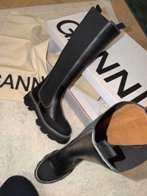 Svarta chunky stövlar från Ganni - Säljer ett par svarta höga stövlar från Ganni med chunky sula och kontrastsömmar. Stövlarna är i en mix av läder och stretchigt tyg, vilket ger en tight passform längs benet. Perfekta för dig som vill ha en edgy och trendig look. Nypris är över 4.500 kr slutsålda
