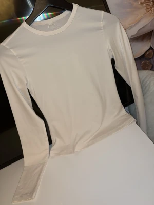 Vit långärmad träningströja H&M - Säljer en vit långärmad träningströja från H&M Move med rund hals och figurnära passform. Tillverkad i ett stretchigt funktionsmaterial som andas, perfekt för träning eller sportaktiviteter. Pris går att diskutera