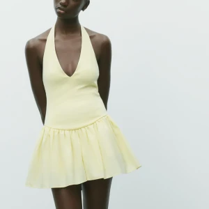 Gul halterneck kortklänning - Supersöt ljusgul kortklänning med halterneck och djup v-ringning. Klänningen har en tight överdel och ett voluminöst, rynkat kjolparti. Knyts i nacken och är ärmlös, perfekt för varma dagar. Tillverkad i mjukt bomullsmaterial för en skön känsla. Endast använd en gång ! Prislappen är ej kvar dock