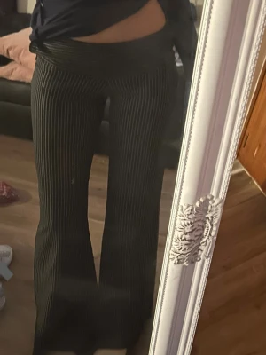 Svarta bootcut byxor med vita ränder - Säljer ett par svarta bootcut byxor med tunna vita ränder. Byxorna har hög midja och är tillverkade i ett stretchigt material som sitter snyggt och bekvämt. Perfekta för dig som gillar en trendig och avslappnad look.