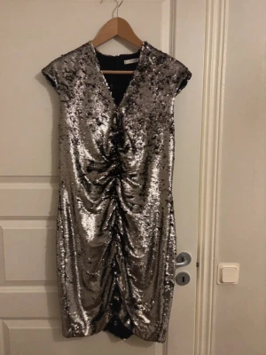 Glittrig silverklänning med paljetter - Snygg kort glittrig klänning i silver med paljetter och rynkade detaljer framtill. V-ringad och med korta ärmar, perfekt för dig som vill sticka ut. Klänningen har en figurnära passform och dragkedja i ryggen. Kolla min profil för fler plagg! 🥰