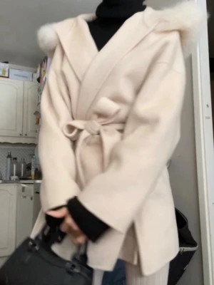 Créme vit kappa med huva och knytskärp - Stilren créme vit kappa med stor huva och fluffig fuskpälsdetalj. Kappan har knytskärp i midjan och vida ärmar för en avslappnad look. Perfekt för lager-på-lager och passar till många outfits.