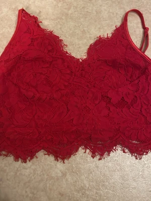 Röd spets bralette med blommönster - Snygg röd bralette i spets med blommönster och tunna axelband. Toppen har en feminin design med vågig spetskant nedtill och är perfekt för att ge outfiten en extra touch. Materialet är mjukt och följsamt för en bekväm känsla.