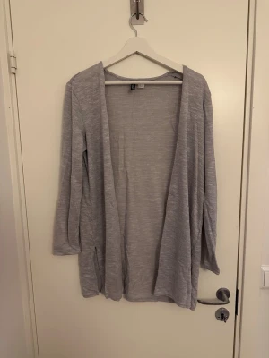 Ljusgrå öppen kofta från H&M - Ljusgrå, tunnstickad öppen kofta från H&M med lång ärm och avslappnad passform. Perfekt att slänga över en t-shirt eller linne. Materialet känns mjukt och lätt, vilket gör den enkel att bära hela dagen.
