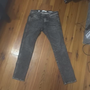 Gråa slim fit jeans - Säljer ett par gråa slim fit jeans med slitna detaljer och klassisk femficksmodell. Jeansen är från Replay och ör anbass modell. Jeansen är knappt använda och är i riktigt bra skick.