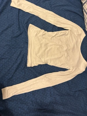 Vit långärmad topp med rund hals - Säljer en enkel och stilren vit långärmad topp med rundad halsringning. Toppen är figurnära och har en mjuk, stretchig känsla som passar perfekt till olika outfits. Materialet känns lätt och bekvämt mot huden. Öppen på halva ryggen 