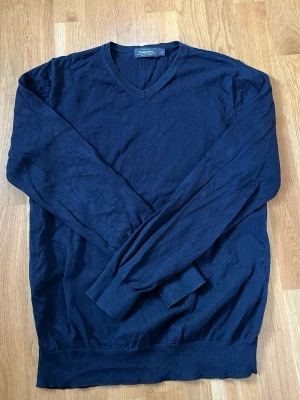 Mörkblå V-ringad tröja Dressmann - Klassisk mörkblå V-ringad tröja från Dressmann i mjuk Supima-bomull. Tröjan har långa ärmar, ribbade muddar och en stilren passform som funkar till många olika looks.