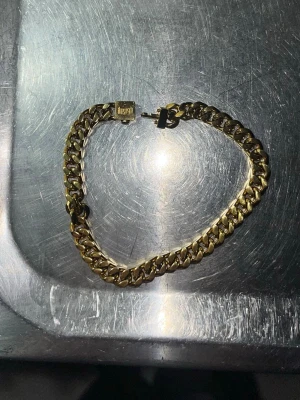 Guldfärgat kedjearmband från kejsar  - Snyggt guldfärgat armband från kejsar  med klassisk kedjedesign. Armbandet har en robust låsdetalj och en stilren, glänsande finish som ger en lyxig känsla. Perfekt accessoar för att lyfta din outfit med en modern touch.