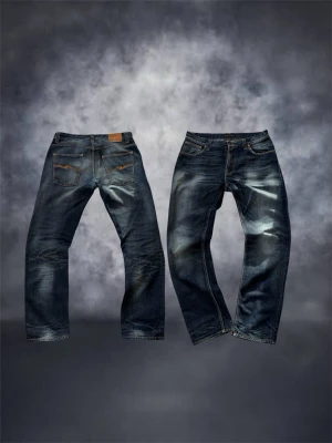 Blå jeans från Nudie Jeans, W34 L34 - Säljer ett par klassiska blå jeans från Nudie Jeans med snygga slitningar och kontrastsömmar. Modellen har raka ben, fem fickor och läderpatch bak i midjan. Tillverkade i slitstark denim, perfekta för en avslappnad stil.