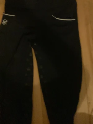 Helskodda ridbyxor  - Snygga svarta ridbyxor från CRW med silikonprint på insidan av benen för extra grepp. Byxorna har vita detaljer vid fickorna och en tight passform som passar perfekt till ridning och träning.