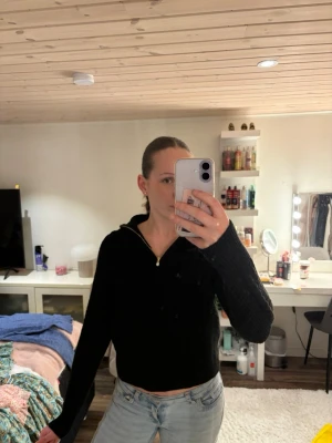 Svart stickad tröja med dragkedja - Svart stickad tröja med halv dragkedja och pärldetalj på dragkedjan. Tröjan har kabelstickat mönster framtill och är långärmad med en lite lösare passform. Perfekt för en trendig och avslappnad look.storlek L men sitter som s