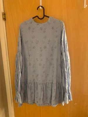 Volangklänning med knyt från NA-KD - Supersöt ljusblå och ljusgul klänning med volangkant och broderade blommor. Långärmad modell med öppen rygg och knytband bak. Båda i storlek S och använda en gång. 350 kr/ per klänning.