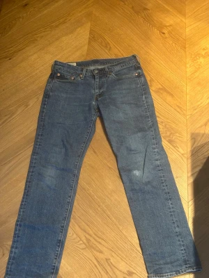 Levi's 501 blå jeans - Klassiska blå jeans från Levi's 501 med rak passform och fem fickor. Jeansen har en tidlös look med kopparfärgade nitar och bälteshällor. Tillverkade i slitstark denim som passar perfekt till en avslappnad stil.