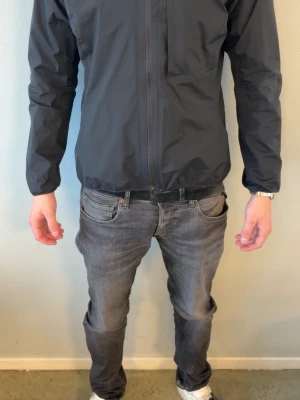 Svart vindjacka med huva från Haglöfs - Snygg svart vindjacka från Haglöfs med minimalistisk design och praktisk huva. Jackan har dragkedja framtill, diskret bröstficka och elastiska muddar. Perfekt för blåsiga dagar och enkel att matcha med olika outfits. OBS liten i stortleken