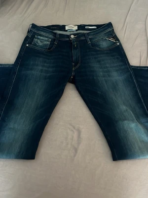 Replay Hyperflex Anbass jeans blå - Snygga blå jeans från Replay, modell Hyperflex Anbass. Jeansen har en slim fit passform, klassiska fem fickor och coola slitningar framtill. Tillverkade i stretchigt material för extra komfort. Perfekta för dig som vill ha en modern och avslappnad stil. Näst in till oanvända. Använda max 5 gånger då jag provade dem.