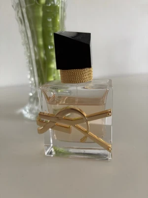 Yves Saint Laurent Libre Eau de Parfum - Snygg parfymflaska från Yves Saint Laurent med guldig logga, transparent glas och svart asymmetrisk kork. Doften är ljusrosa och flaskan har en lyxig känsla med detaljer i guld och struktur på halsen. Finns tyvärr ingen kartong till. Stl på flaskan är 30 ml och det finns 25 ml kvar.