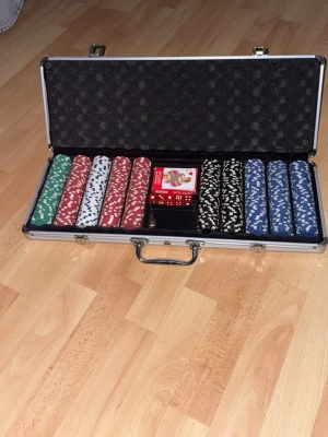 Poker set i aluminiumväska - Säljer ett komplett pokerset i en silverfärgad aluminiumväska. Innehåller pokerchips i färgerna grön, röd, vit, svart och blå, en kortlek samt röda tärningar. Perfekt för pokerkvällar med vänner. Väskan har handtag och lås för enkel transport.