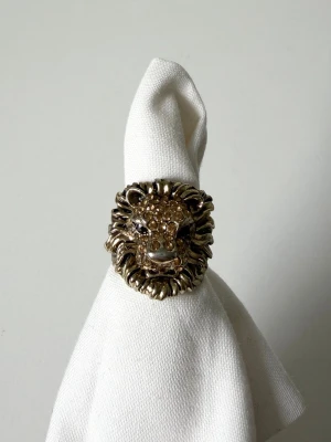 Guldfärgad ring med lejonhuvud - Cool ring i guldfärgad metall med ett detaljerat lejonhuvud. Lejonets ansikte är dekorerat med små gnistrande stenar. Ringen har en robust och chunky design som verkligen sticker ut och är cool att ha i stack 🤍