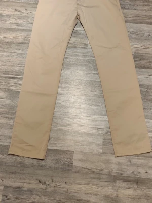 Väldigt fina Armani chinos - Snygga beige chinos från Emporio Armani med klassisk rak passform. Byxorna har diskret logga ovanför bakfickan och är tillverkade i ett mjukt bomullstyg som känns skönt mot huden. Perfekta för en stilren och avslappnad look.     Det är storlek 34/34 och de kostar 4000 i butik, de är helt oanvända och jag fick dem i present. De är äkta vilket du kan se på bilden.