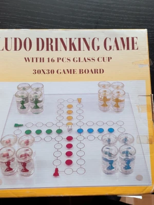 Ludo Drinking Game med glas - Roligt Ludo Drinking Game med 16 små glas och en spelplan i glas, 30x30 cm. Perfekt för spelkvällar med vänner där varje spelpjäs är ett shotglas i olika färger: röd, grön, blå och gul. Inkluderar även tärning.