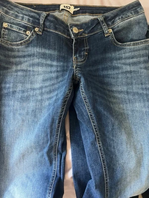 Blå bootcut jeans från 157 - Snygga blå bootcut jeans från 157 med klassisk femficksdesign och ljusa slitningar framtill. Jeansen har normal midja och är tillverkade i denim med lätt stretch för skön passform. Perfekta för en avslappnad och trendig look.