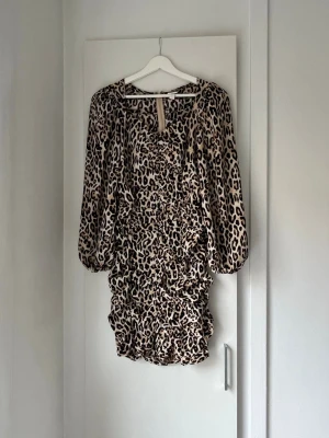 Leopardmönstrad kort klänning - Snygg kort klänning med leopardmönster och långa puffärmar. Klänningen har rynkade detaljer framtill och dragkedja i ryggen. Perfekt för dig som vill sticka ut med en trendig look.
