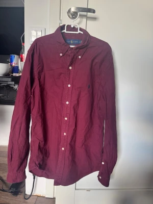Vinröd skjorta från Ralph Lauren - Vinröd långärmad skjorta från Ralph Lauren. Otroligt snygg och passande inför en magisk sommar 