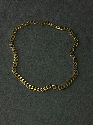 Guld Cubansk Kedja 50cm 9mm i Rostfritt Stål - 50cm Långt 9mm tjockt halsband i guld färg. Stilrent halsband med breda, platta länkar i guldfärgat stål. Kedjan har en klassisk karbinhake och en glansig finish som ger en modern vibe. Perfekt för att lyfta din outfit med en edgy touch.