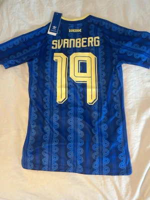 Blå Sverige fotbollströja Adidas - Sverige VM tröja 2026 fotbollströja med gula detaljer, nummer 19 och namnet Svanberg på ryggen. 