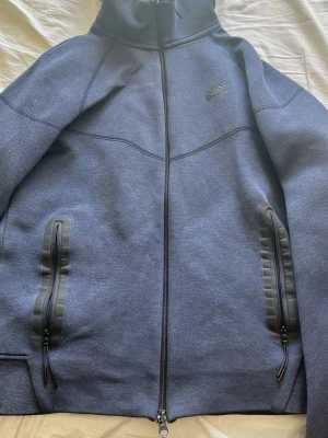 Mörkblå Nike tech fleece med dragkedja - Snygg mörkblå hoodie från Nike med hel dragkedja framtill och två dragkedjeförsedda fickor. Tillverkad i mjukt material och har en stilren look med diskret Nike-logga på bröstet. Perfekt för en sportig och avslappnad stil. Passar på dig som är 180